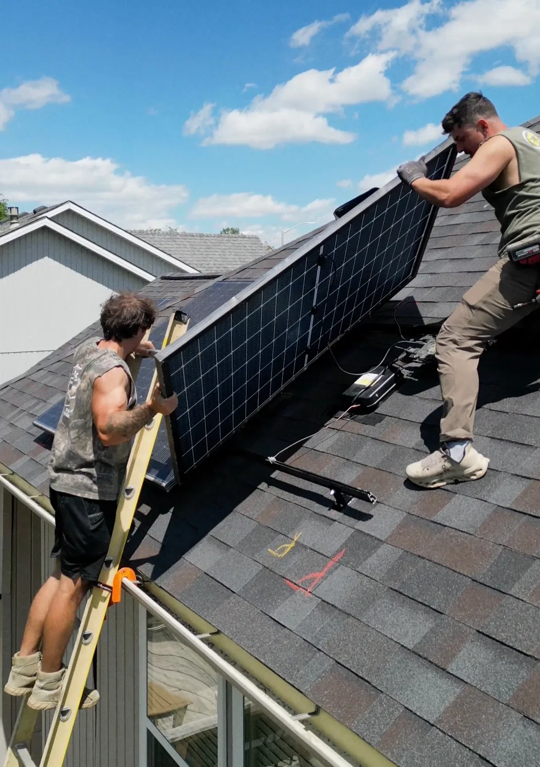 Two Solar Scapes technicians lifting a solar panel into place on a shingle roof