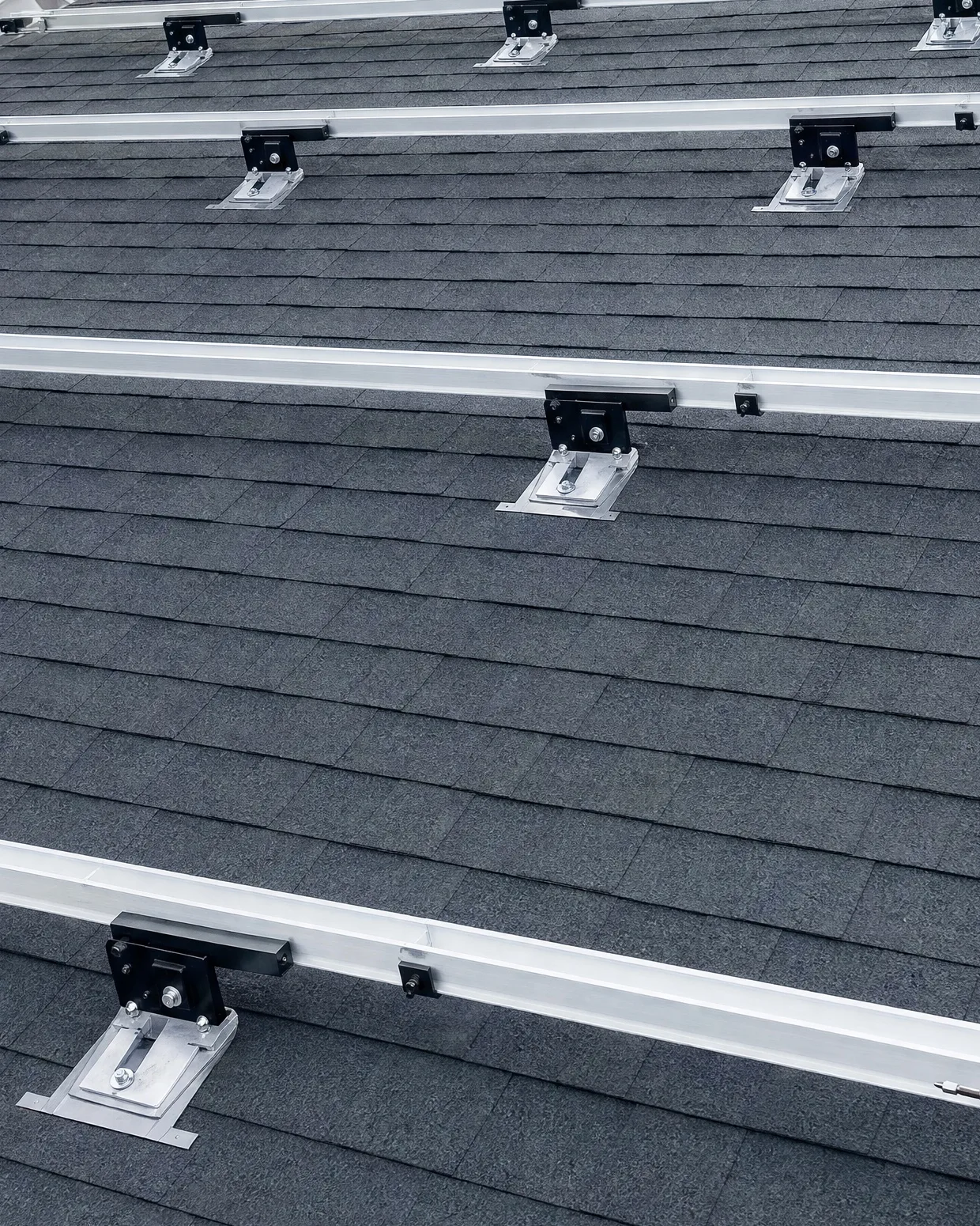 Rows of solar racking rails bolted to flashed roof attachments on a shingle roof
