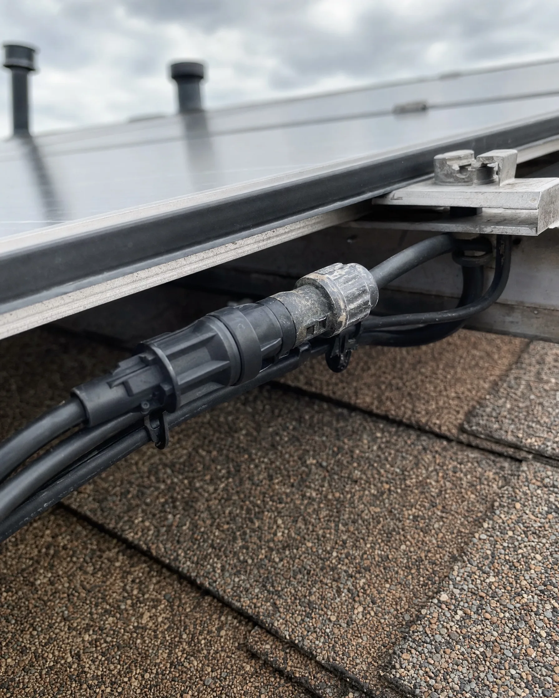 Weathered solar connector and wiring clipped under a rooftop panel
